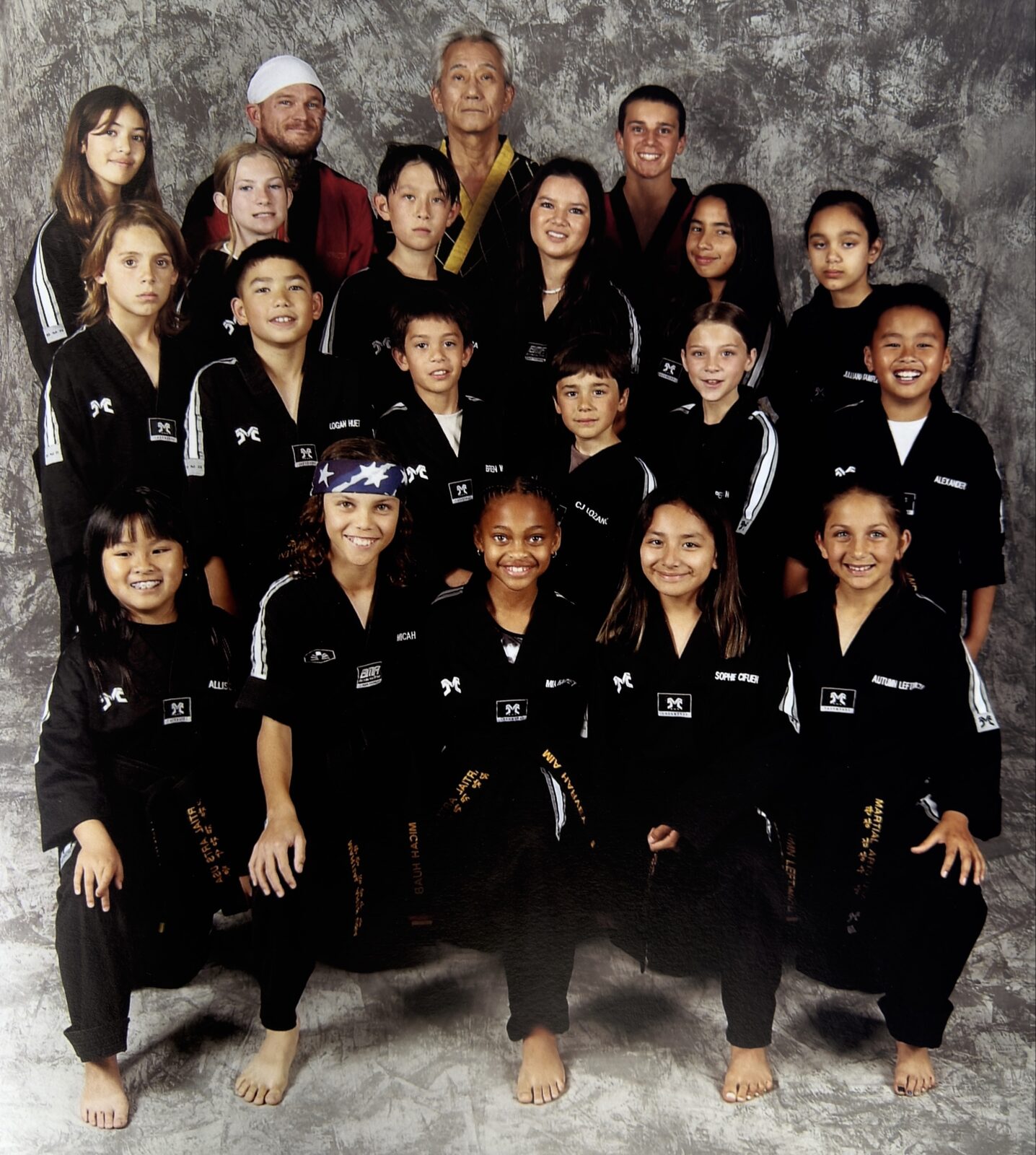 Group photo of youth martial arts students in black doboks with instructors, studio portrait