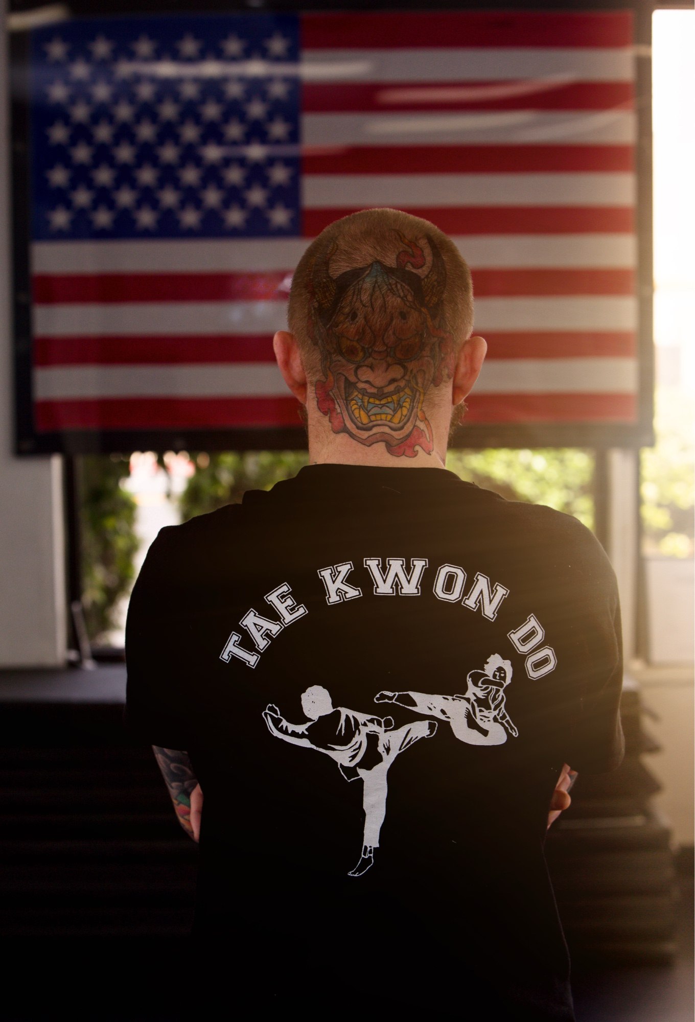 Shaun Anderson standing with his back to the camera in a Tae Kwon Do shirt, facing an American flag